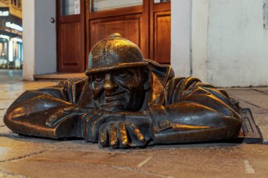 Bratislava, Slovakya 'nın düşük açılı Cumil heykeli geçen kalabalığa gülümsüyor. Kanalizasyon kapağında şapkası olan dinlenen bir lağım işçisini gösteren bronz bir sanat eseri..