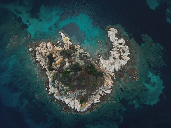 Yunanistan 'ın Chalkidiki yarımadasındaki Akdeniz' de yeşil bitki örtüsüyle küçük kayalık adanın üzerinde insansız hava aracı manzarası