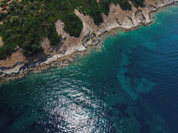 Yunanistan 'ın Chalkidiki yarımadasındaki Akdeniz' de yeşil bitki örtüsü bulunan küçük ada kayalık kıyı şeridi üzerindeki insansız hava aracı manzarası