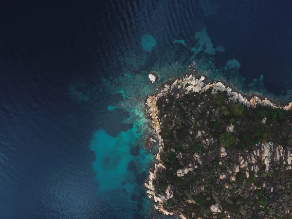 Yunanistan 'ın Chalkidiki yarımadasındaki Akdeniz' de yeşil bitki örtüsü ve kayalık kıyı şeridi bulunan küçük adanın üzerinde insansız hava aracı manzarası.