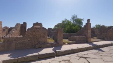 Archaeological area of Pompeii, Italy POV walking on Roman architecture empty main street with city block house remains.