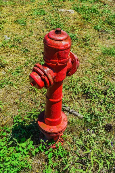 Red metal above ground water fire hydrant piping point against green vegetation at a rural environment.