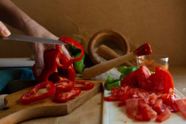 Mutfak bıçağıyla kesilmiş kırmızı biber ve ahşap tahtada parçalanmış domates.