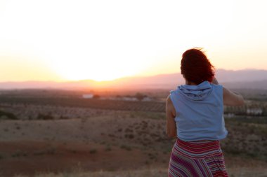 Kızıl saçlı, mavi kazaklı, gün doğumunda fotoğraf çeken tanınmamış bir kadın.