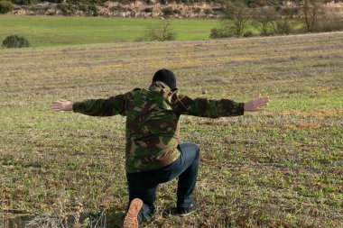 Military man in jeans and balaclava detained with his arms raised in the mountains