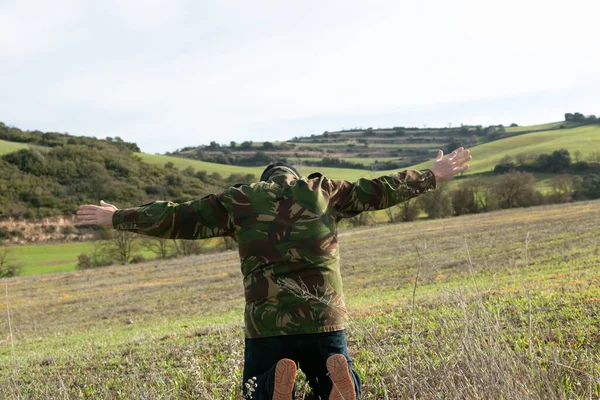 Military man in jeans and balaclava detained with his arms raised in the mountains