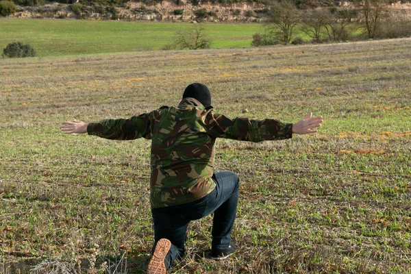 Military man in jeans and balaclava detained with his arms raised in the mountains Stock Image