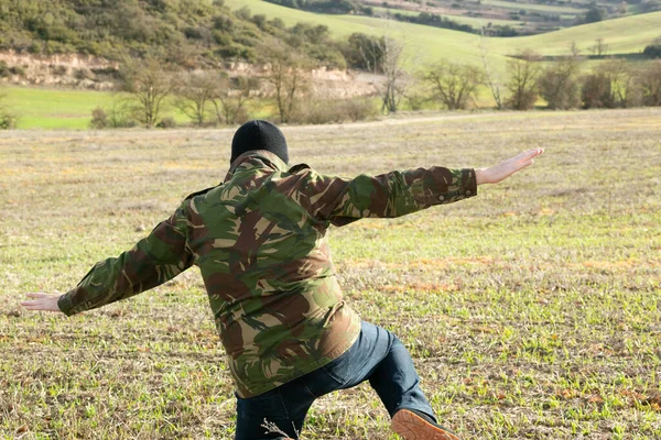 Military man in jeans and balaclava detained with his arms raised in the mountains