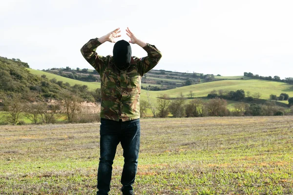 Military man in jeans and balaclava detained with his arms raised in the mountains Royalty Free Stock Photos