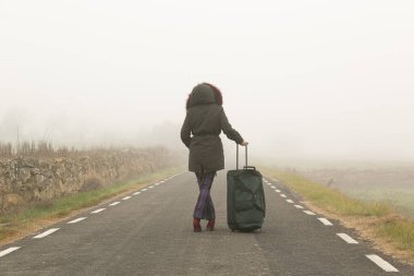 Tanımlanamayan bir kadın, elinde bavuluyla soğuk ve sisli bir dağda yürüyor.