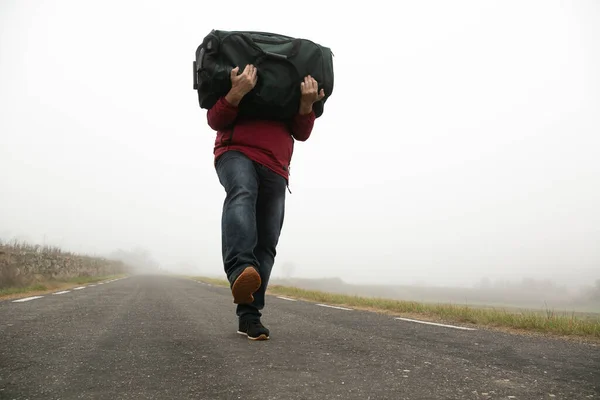 Kot pantolonlu bir adam ve sisli yolda kırmızı Mackintosh, sırtında ağır bir bavul tanınmaz halde.
