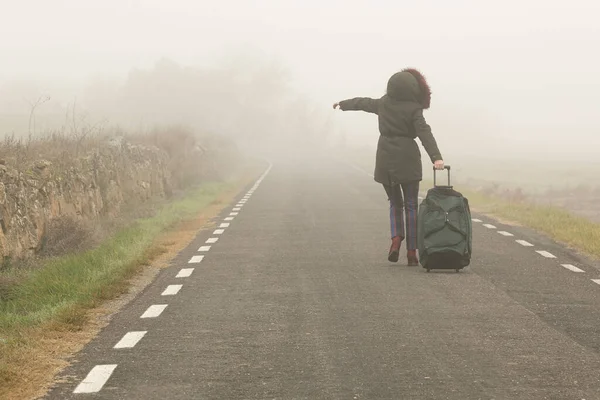 Unerkennbare Frau läuft mit Koffer in der Hand auf kalter und nebliger Bergstraße — Stockfoto