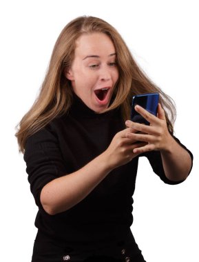 Elinde cep telefonuyla gülümseyen genç sarışın kız beyaz arka planda siyah kazak giyiyor.