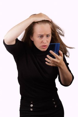 Elinde cep telefonuyla gülümseyen genç sarışın kız beyaz arka planda siyah kazak giyiyor.