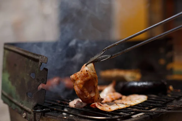 Metal tongs moving smoked pork bacon on outdoor barbecue outside the house. Family Food Day with outdoor barbecue activity.