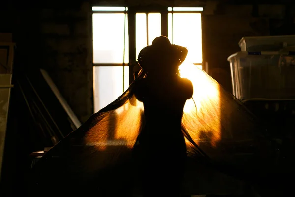 Woman backlit in window of old industrial building playing with fabrics