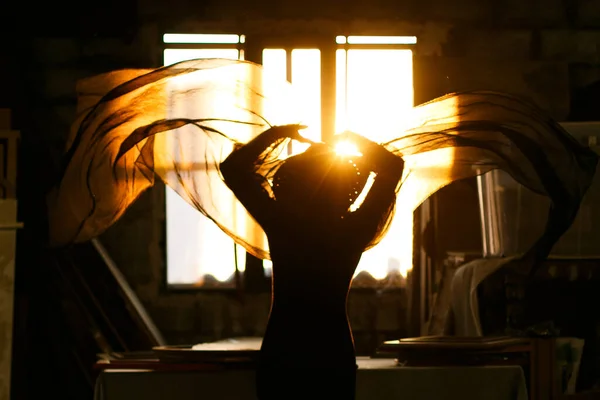 Woman backlit in window of old industrial building playing with fabrics