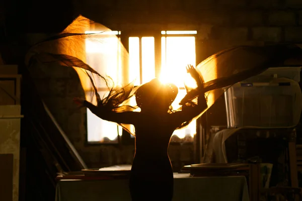 Woman backlit in window of old industrial building playing with fabrics