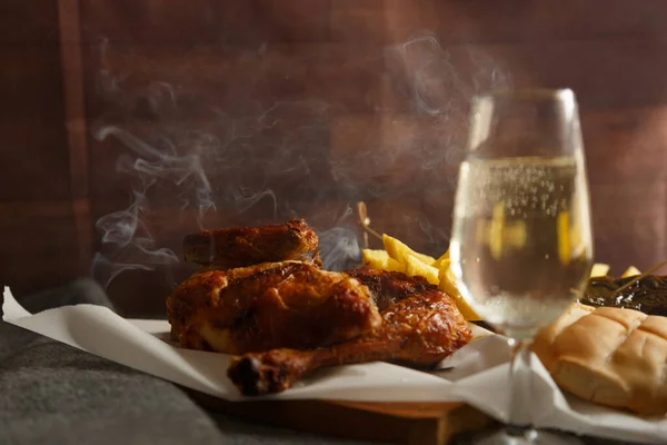 Freshly cooked roast chicken with potatoes, on a wooden table about to be served.