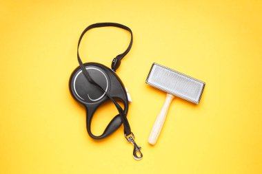 Sarı arka plandaki köpekler için siyah geri çekilebilir tasma ve fırça..