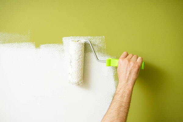 Ролик краски в руке человека, перекрашивающего стену, живопись.