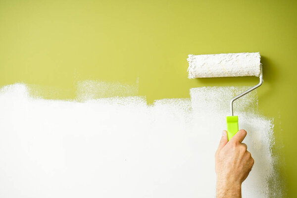 Paint roller in the hand of a man repainting the wall. Space for text.
