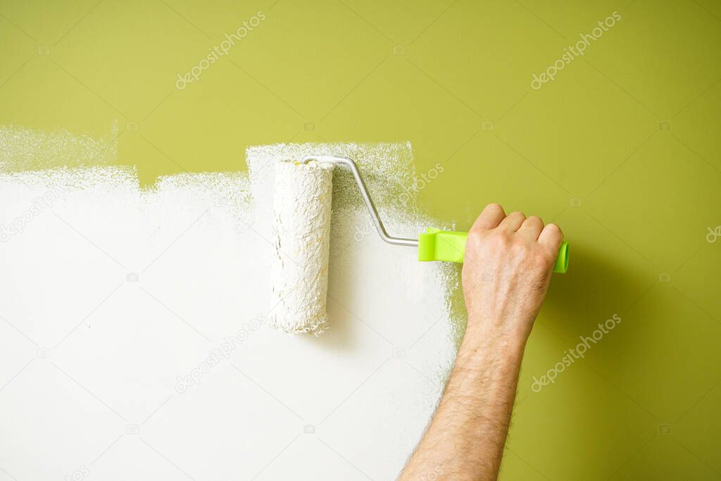 Paint roller in the hand of a man repainting the wall, painting work.