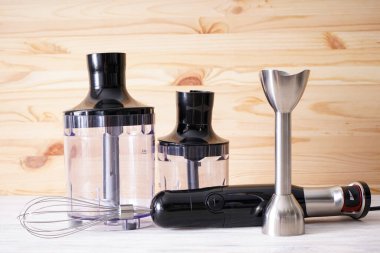 Black plastic electrical hand blender with stainless steel body and accessory on wooden background.
