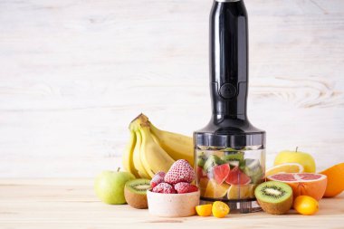 Hand blender and accessories with sliced fruit on a wooden background, place for text. Close up.	