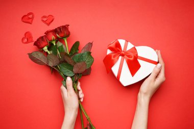 Sevgililer Günü konsepti. Kırmızı arkaplanda kırmızı güller ve kalp şeklinde beyaz bir hediye kutusu var. Üst görünüm.