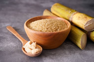 Granüle kahverengi şeker, şeker kamışı ve gri arka planda yeşil yaprak. Yakın plan..