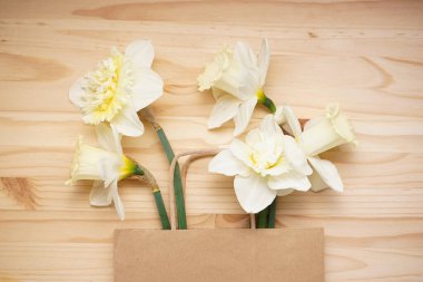 Sarı nergis çiçekleri ve tahta arka planda kağıt torba..