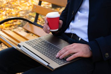 Sonbahar parkında elinde kahve ve dizüstü bilgisayar olan genç bir adam..