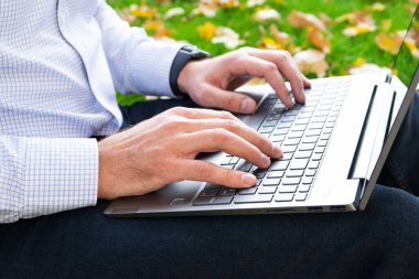 Genç adam parkta dizüstü bilgisayar kullanıyor. Yakın plan..