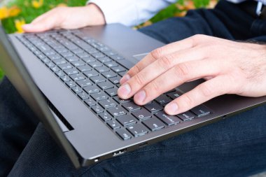 Genç adam parkta dizüstü bilgisayar kullanıyor. Yakın plan..