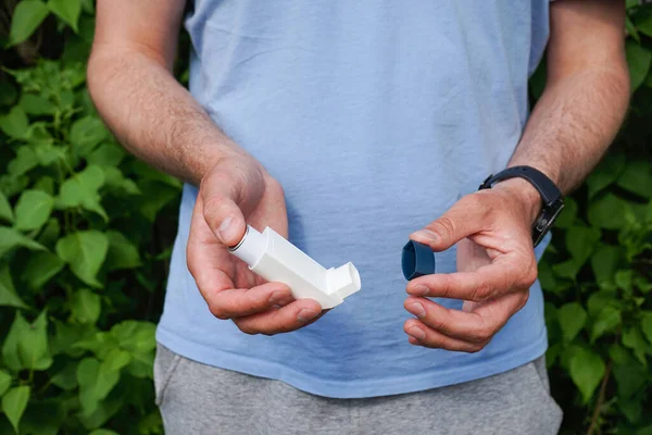 Health and medical concept. Male hands holding asthma inhaler on attack outdoor.