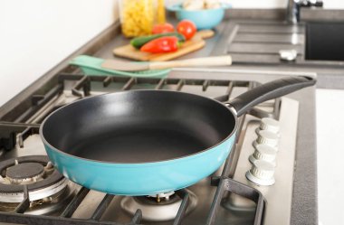 New frying pan on the stove. Fresh vegetables lie near the frying pan on the countertop.