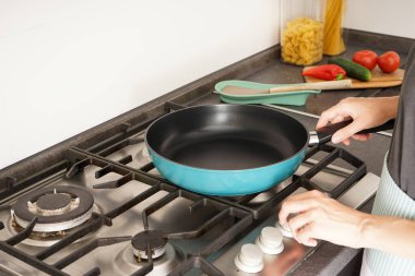 Young woman holding a new frying pan in her hands on the background of the kitchen and vegetables