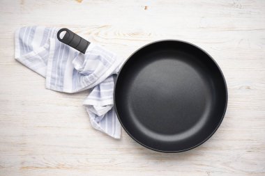 New frying pan and kitchen towel on a wooden background. Top view, flat lay.