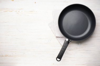 New frying pan and kitchen towel on a wooden background, space for text. Top view, flat lay.