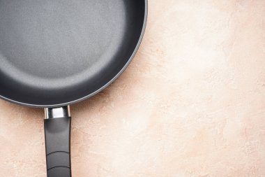 New frying pan and kitchen towel on a beige background, space for text. Top view, flat lay.