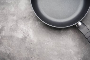 Gri arka planda yeni bir tava ve mutfak havlusu. Mesaj için yer var. Üst manzara, düz uzanma.