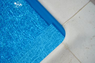 Swimming pool with blue water outdoors with stone gray edge, close-up. Top view.