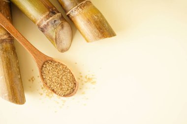 Granulated brown sugar, sugarcane on a yellow background, flat lay. Space for text.