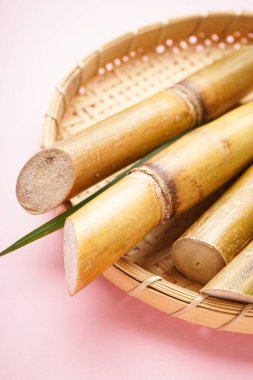 Sugar cane and green leaf in a wooden tray on a pink background. Vertically.