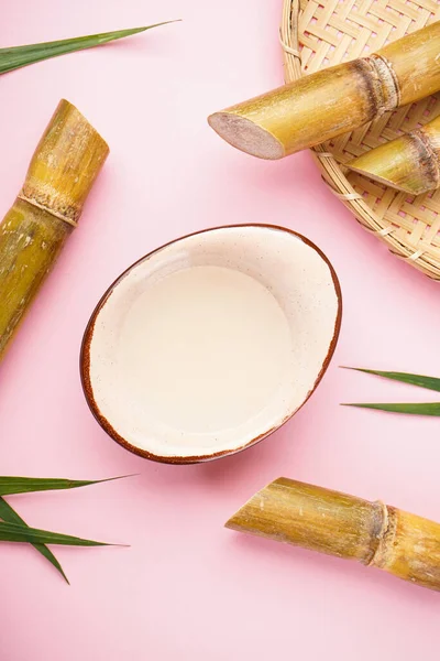 Fresh sugar cane juice and sugar cane on a pink background, vertically, top view.