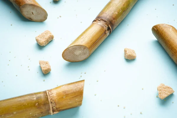 Sugar cane and brown sugar pieces on blue background, close-up.