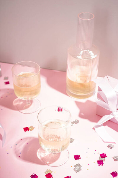 Champagne in glasses and a gift on a pink background. Vertically.