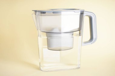 Su filtresi sürahi ve sarı arka planda bir bardak su, yakın plan..