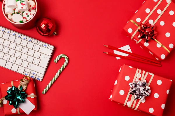 Klavye ve Noel hediyeli çalışma alanı ve kırmızı zemin üzerinde şeker kamışı düz bir görünüm, kopyalanmış uzay, kopyalanmış noel tatili konsepti online alışveriş